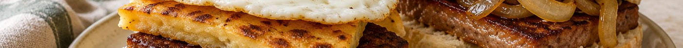 Two morning rolls filled with square sausage, one with egg and potato scone and one with onions and sauce.