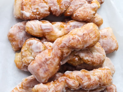 A batch of glazed Yum Yum doughnuts on a white surface.