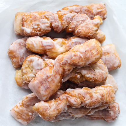 A batch of glazed Yum Yum doughnuts on a white surface.